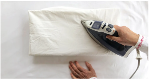 Person ironing white bed sheets on a flat ironing board