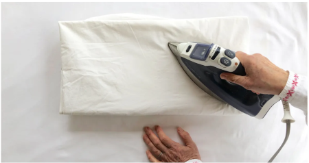Person ironing white bed sheets on a flat ironing board